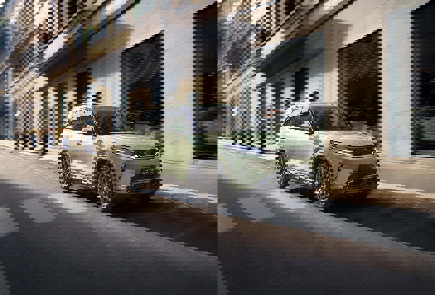 En hvid SUV kører langs en bygade med høje bygninger på en klar dag, hvilket skaber et levende og dynamisk bybillede.