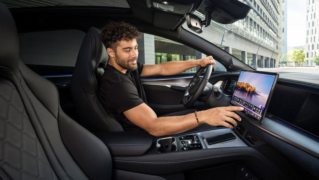 Mand sidder i bilens førersæde og interagerer med den store centrale berøringsskærm på instrumentbrættet.