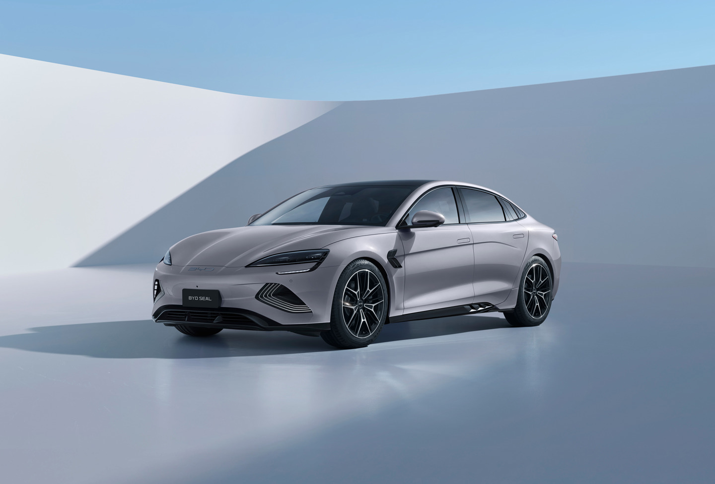 En sølvfarvet elbil i sedan-stil parkeret i et minimalistisk, moderne udendørs miljø under en klar blå himmel.