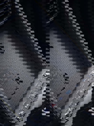 Et detaljeret nærbillede af en mørk, struktureret overflade med åbninger og netmønstre, der tyder på, at den er en del af elegant elektronisk udstyr eller computerudstyr.