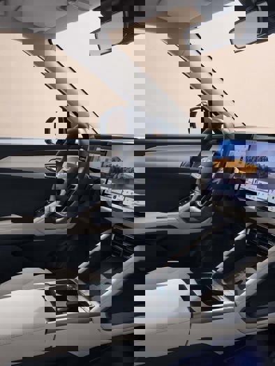 En person sidder i førersædet af en bil og holder en smartphone, begge hænder er synlige på rattet. Billedet fremstår klart og tydeligt.