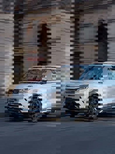 En hvid SUV kører langs en gade i byen, omgivet af dynamisk bylandskab og levende bevægelse.