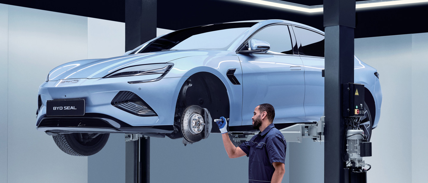 En mekaniker inspicerer en blå BYD Seal-bil, der er løftet op på en hydraulisk platform i en moderne garage.