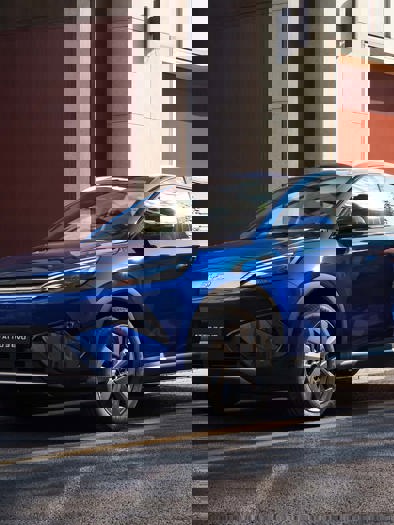 En blå SUV kører på en gade i byen.