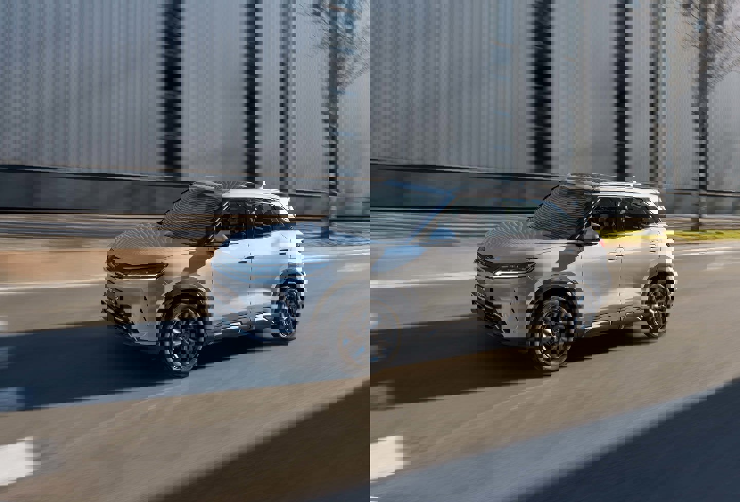 En hvid SUV kører langs en bygade og passerer moderne bygninger i baggrunden, hvilket skaber en livlig byatmosfære.