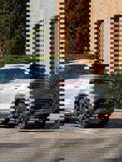 En hvid SUV holder parkeret på en gade omgivet af træer og bygninger i baggrunden.