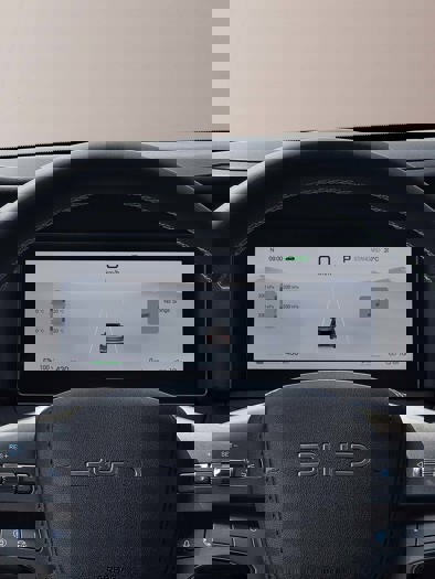 Et nærbillede af en bils instrumentbræt og rat med en central touchscreen, der viser et kort, og som fremviser moderne interiørdesign og teknologi.